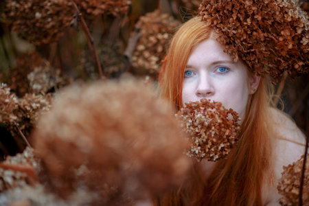 Portrait of a young lovely red-haired girl with a clear shoulders peering out between parched...