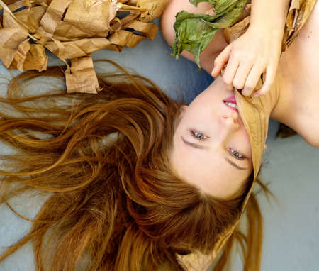 unusual remarkable oblique diagonal portrait with dry plant parts of a beautiful sensual seductive astonishing, young sexy woman with red brown hair artfully decorated between banana leavesの写真素材