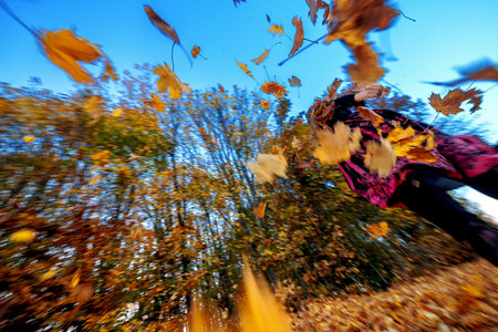 young woman runs in autumn and whirls up the autumn leaves, leaves fly in the sky, copy space
