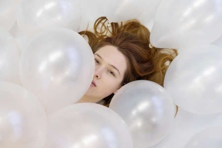 View from above beautiful young sexy redhead woman face between white iridescent balloons, beauty fashion concept.の写真素材