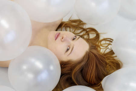 Portrait art view from above to beautiful young sexy woman face with red hair between white iridescent balloons, beauty fashion conceptの写真素材