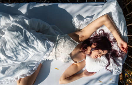 View from above to an attractive, young, sexy dark brown long haired woman in bed sleeping in the morning sun, copy space.の写真素材