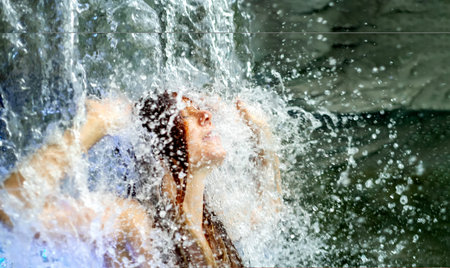 beautiful young sexy redhead woman under the splashing water of the waterfall in the spa wellness...
