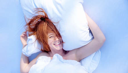 attractive young sexy redhead woman laughs and holds pillow in sunlight, upside down,の写真素材