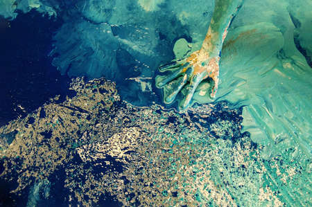 colorful painted female hand of a woman in green, blue, white liquid color that looks like a surreal coastal landscape from above, copy spaceの写真素材