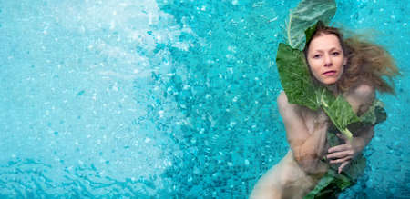 wide banner portrait of beautiful sexy naked woman in water with green wet leaf near face. soft skin, healthy fresh look. natural beauty. concept of skincare, wellness, spa, copy spaceの写真素材