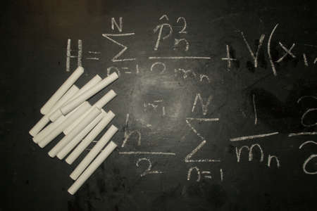 Close up Image of a pile/bunch of white chalks on a blackboard with a written mathematical formulaの写真素材