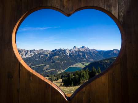 Tannheimer Tal panorama with view on the Haldensee seen through a wooden heartの写真素材