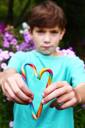 preteen boy with rainbow candy sticks on the summer blossom garden backgroundの写真素材