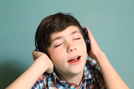 preteen handsome boy with headphones listen to popular mp3 music on computer close up expression portrait isolated on blueの写真素材