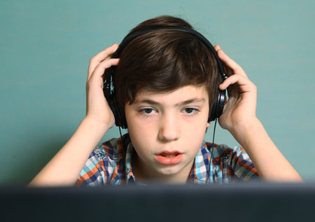 preteen handsome boy with headphones listen to popular mp3 music on computer close up expression...
