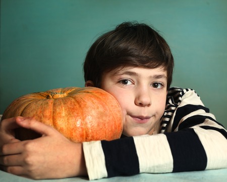 preteen handsome boy with big orange pumpkin close up portrait on blue wall backgroundの写真素材