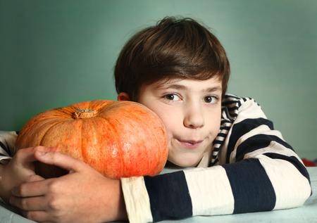 preteen handsome boy with big orange pumpkin close up portrait on blue wall backgroundの写真素材