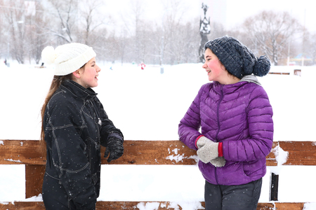 two teenager girl in knitted woolen hat and down overall and jacket on the skating ring talk on smile on the snowy white backgroundの写真素材