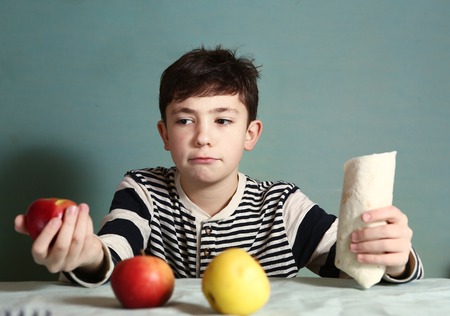 preteen handsome boy make choice between healthy food apples and fast food caesar rollの写真素材