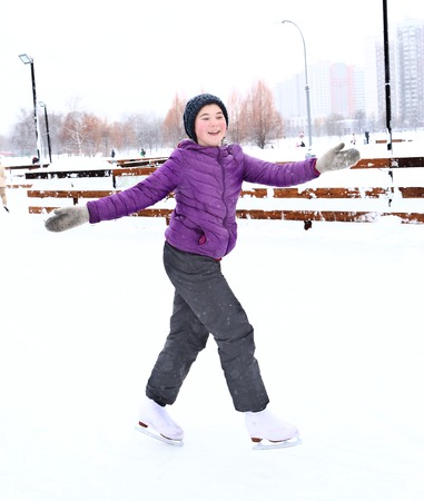 teen pretty girl in dawn jacket and knitted hat skating on the ice skating rink on the snowy park backgroundの写真素材