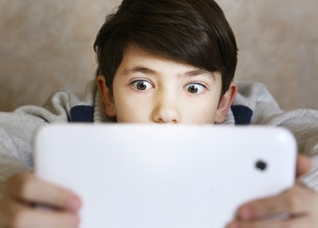 preteen handsome boy with bad gaming habit play computer game on his tablet close up portraitの写真素材