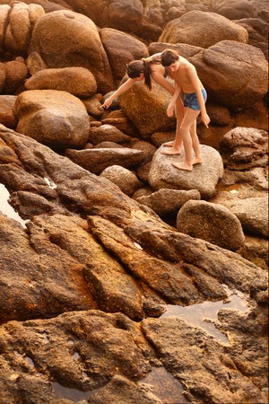 boy in swimming trunks climbing rocks on the stony thai beachの写真素材