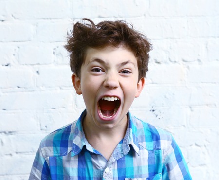 preteen handsome boy shouting yelling close up portrait on the white wall backgroundの写真素材