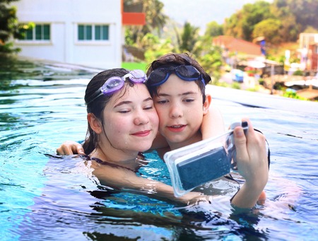 teen siblings brother and sister take photos with underwater cover camera close up portrait in open air thai swimming poolの写真素材