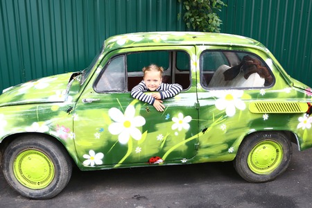 blond smiling preteen girl in old painted with fowers car cose up portraitの写真素材