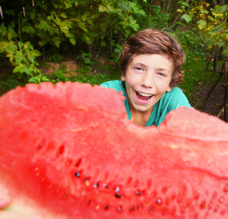 preteen boy with water melon bitten slice in the summer garden smilingの写真素材