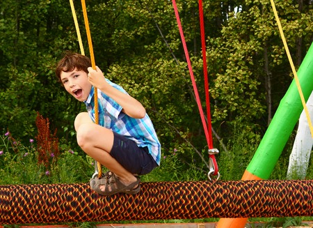 preteen happy boy in outdoor amusement park attraction log swing close up laughing smiling portraitの写真素材