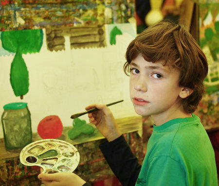 preteen handsome boy in art class have painting lesson with brush and easel close up photoの写真素材