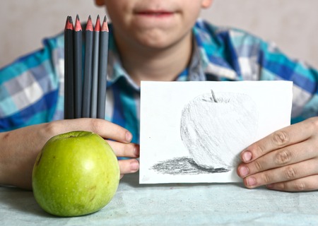 apple and drawing in kids hands with different shade coal crayons set close up photoの写真素材