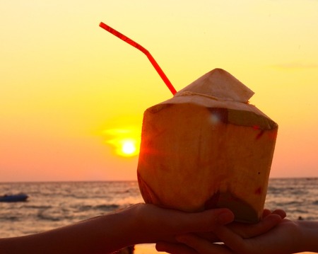 hands hold coconut with straw on the sunset backgroundの写真素材