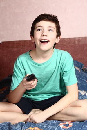 preteen boy watch movie with remote control laughing smileの写真素材