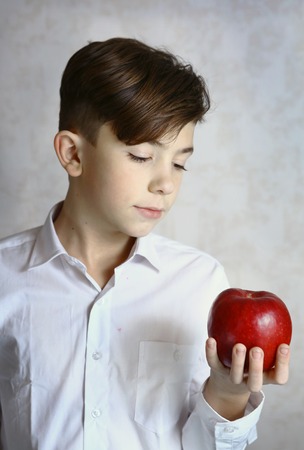 teenager boy hold red apple close up photo on white wall backgroundの写真素材