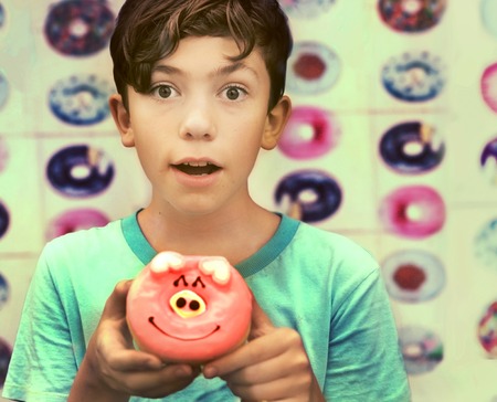 teenage european boy with doughnut on confectionery background close up photoの写真素材