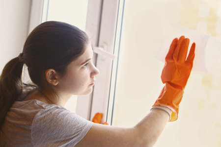 teen girl in orange rubber gloves cleaning window close up portrait