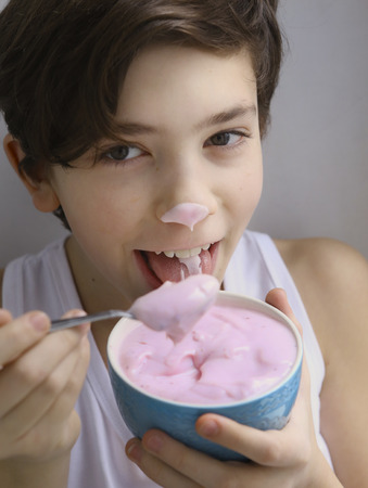 teenager boy eating pink yogurt from the bowl close up smiling portraitの写真素材