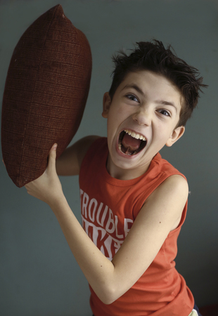 teenager mischivous boy fighting with pillow open mouth close up portraitの写真素材