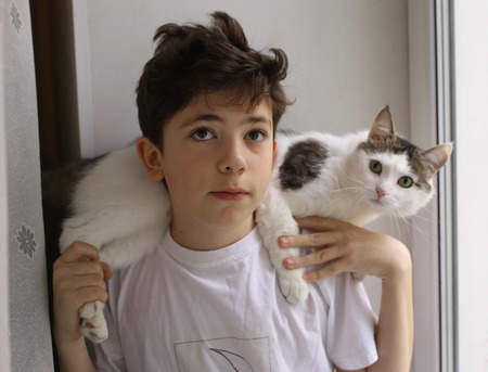 teenager boy with cat on his shoulders close up photo on window backgroundの写真素材