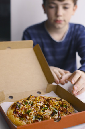 boy grab chicken barbeque pizza in box close up photoの写真素材