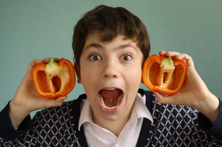 teenager boy with cut bulgarian paprica red sweet pepper earsの写真素材