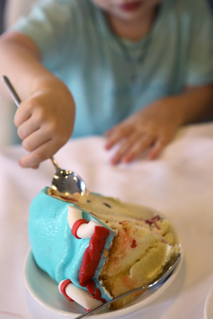 piece of birthday kids cake cut on the plate with teaspoon in kid hands eating close up photoの写真素材