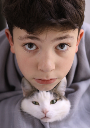 teen boy with cat wrap in rug close up winter cosy photoの写真素材