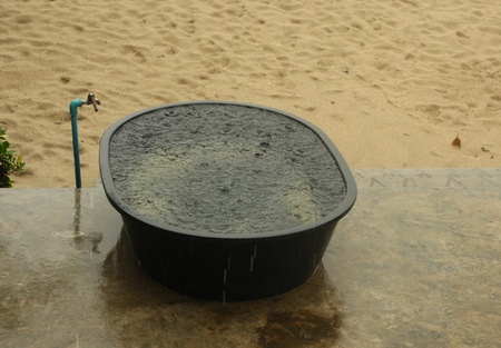 raining on sandy beach with water full basin with rain dropsの写真素材
