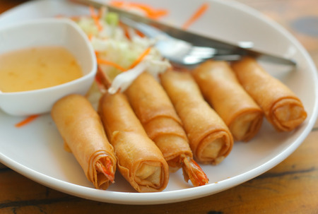 top view photo of roasted spring rolls with shrimps sore and sweet sauce knife and salad on the wooden table close upの写真素材