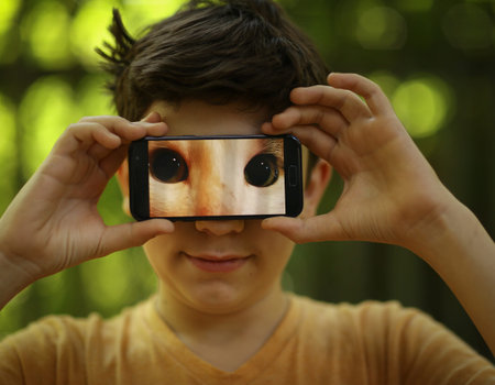teenager boy make funny picture with cats eyes on cell phone outdoor summer photo