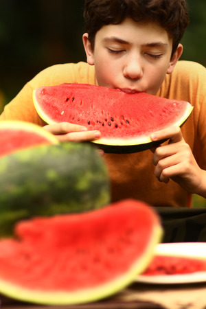 teenager boy eating cut water melon close up photo on green garden backgroundの写真素材