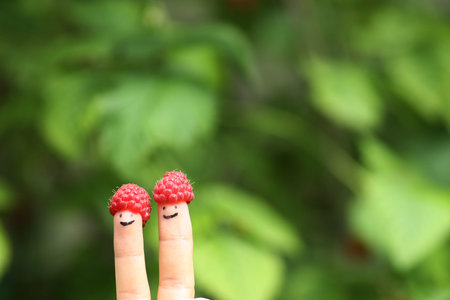 two fingers in funny raspberry hats on green bush background close up photo