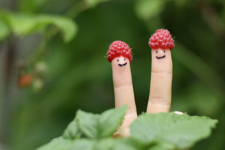 two fingers in funny raspberry hats on green bush background close up photo