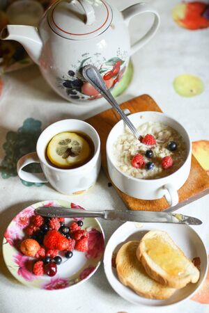 breakfast still life with oatmeal, seasonal berries, roasted toasts with lemon jam cup of tea spoon and knife close up vertical photoの写真素材