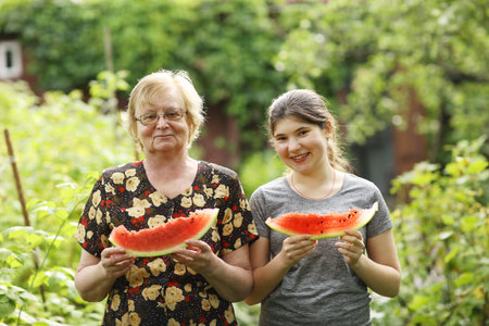 teen girl and grandma with cut water slice melon close up photo on green garden background