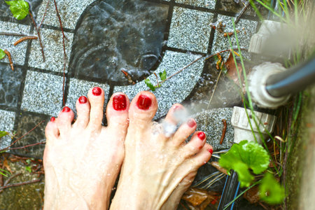 woman feet with red nail enamel washing with water pate on garden tale background